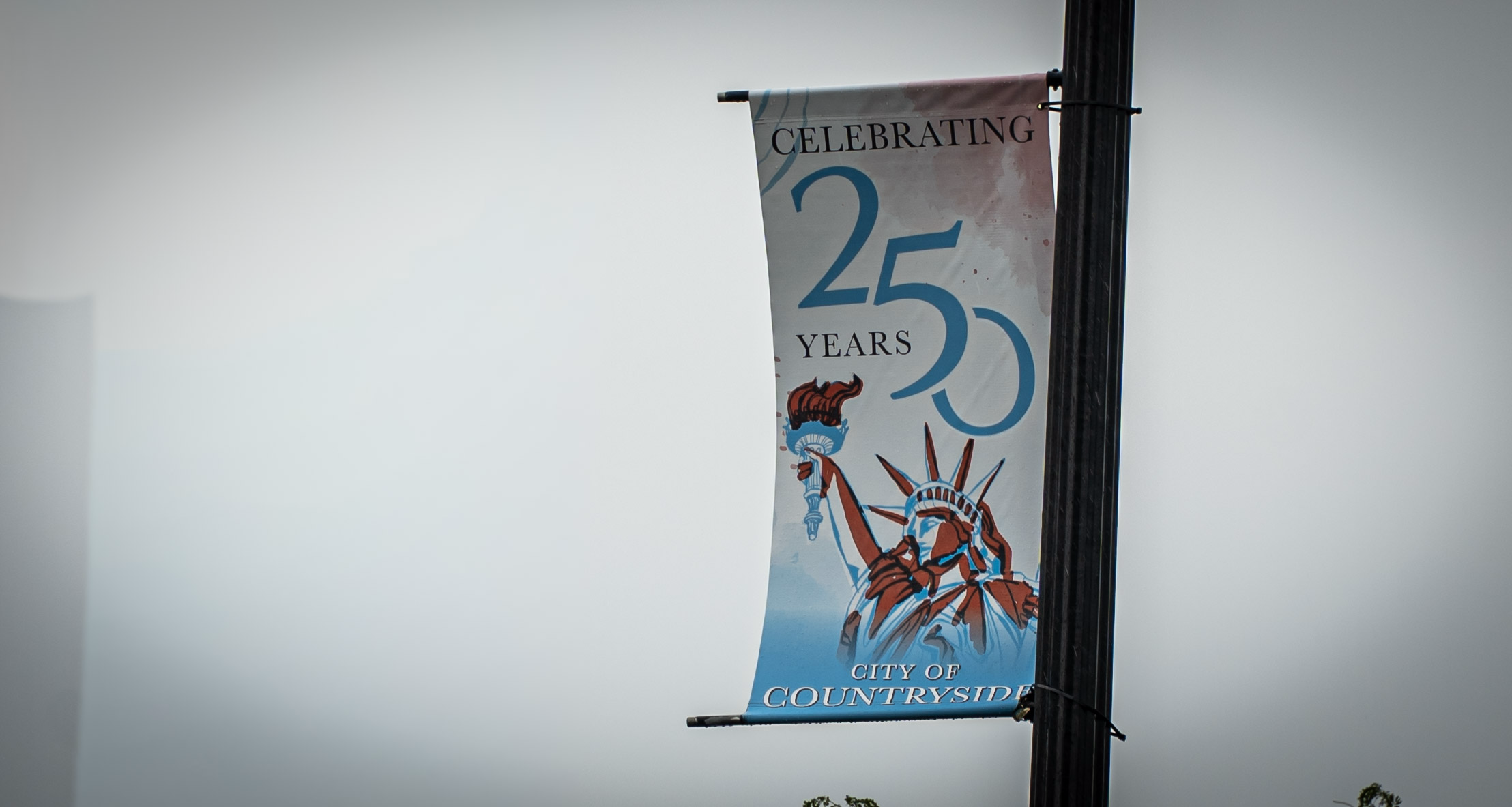 A street banner attached to a lamp post reads "Celebrating 250 Years" and "City of Countryside," with a illustration of the Statue of Liberty against a light blue background.
