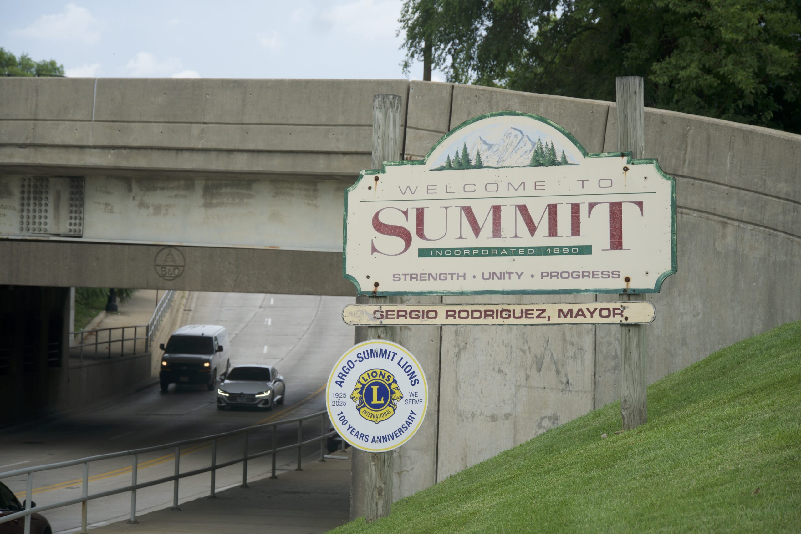 Welcome sign for the Village of Summit beside a road leading under an overpass.