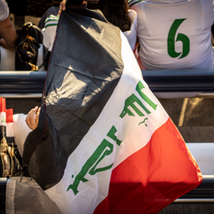 Soccer fan wearing an Iraqi flag in the stadium stands during a match.