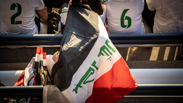 Soccer fan wearing an Iraqi flag in the stadium stands during a match.