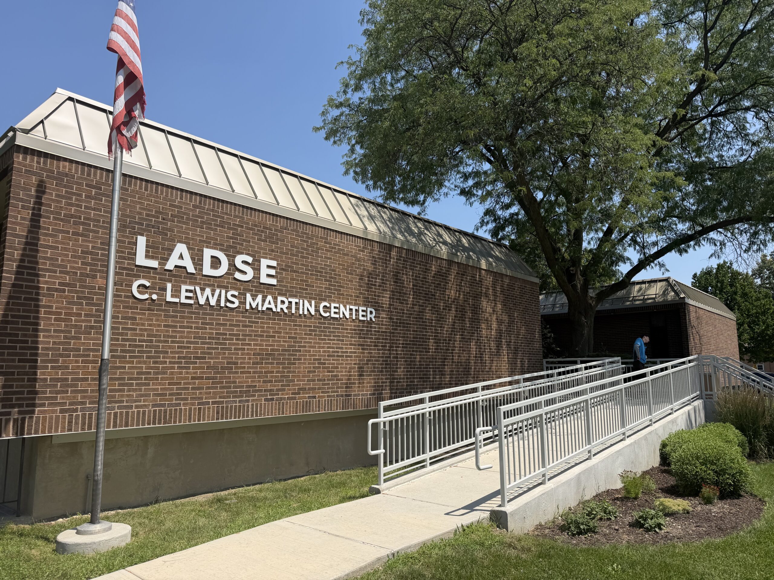 Brick LADSE C. Lewis Martin Center building with an American flag, accessible ramp, and large tree outside.