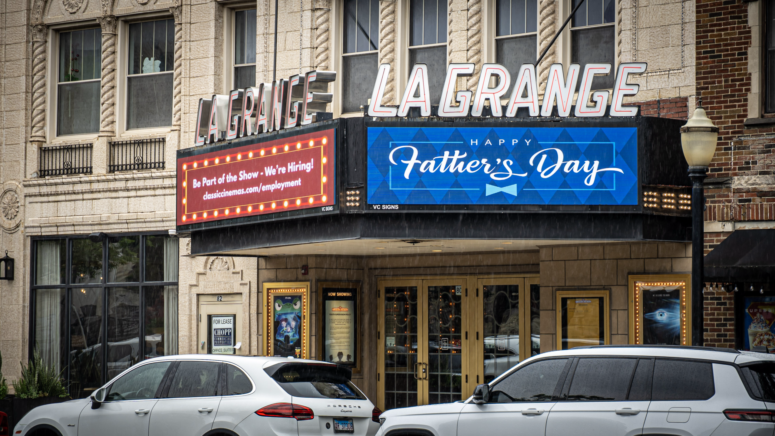 Front entrance of the LaGrange Theater with a marquee displaying "Happy Father's Day" and a hiring announcement, with cars parked along the street.
