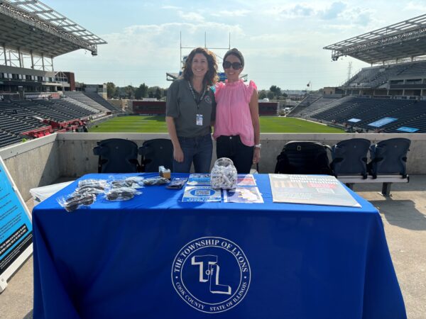 Elyse Hoffenberg and Molly Price stand behind a voter registration table at the SeatGeek Stadium concourse before a Chicago Hounds game.