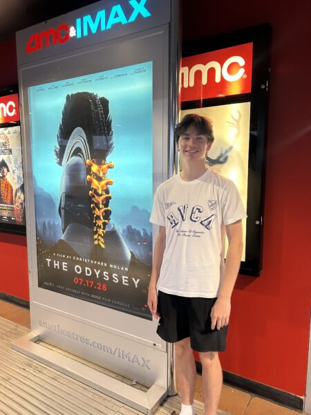 Man stands in front of a sign for 'The Odyssey" with AMCIMAX at the top of the sign.