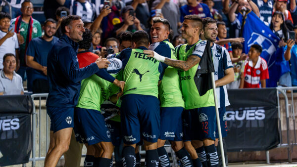 Monterrey players and staff celebrate together near the sideline as a large crowd of fans cheers behind them.
