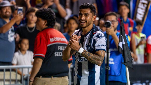 A smiling Monterrey player claps near the corner flag while spectators and security staff watch from behind.